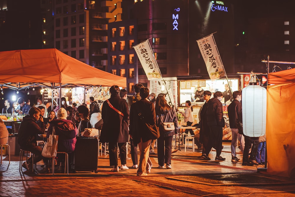 a group of people standing around a food stand at night