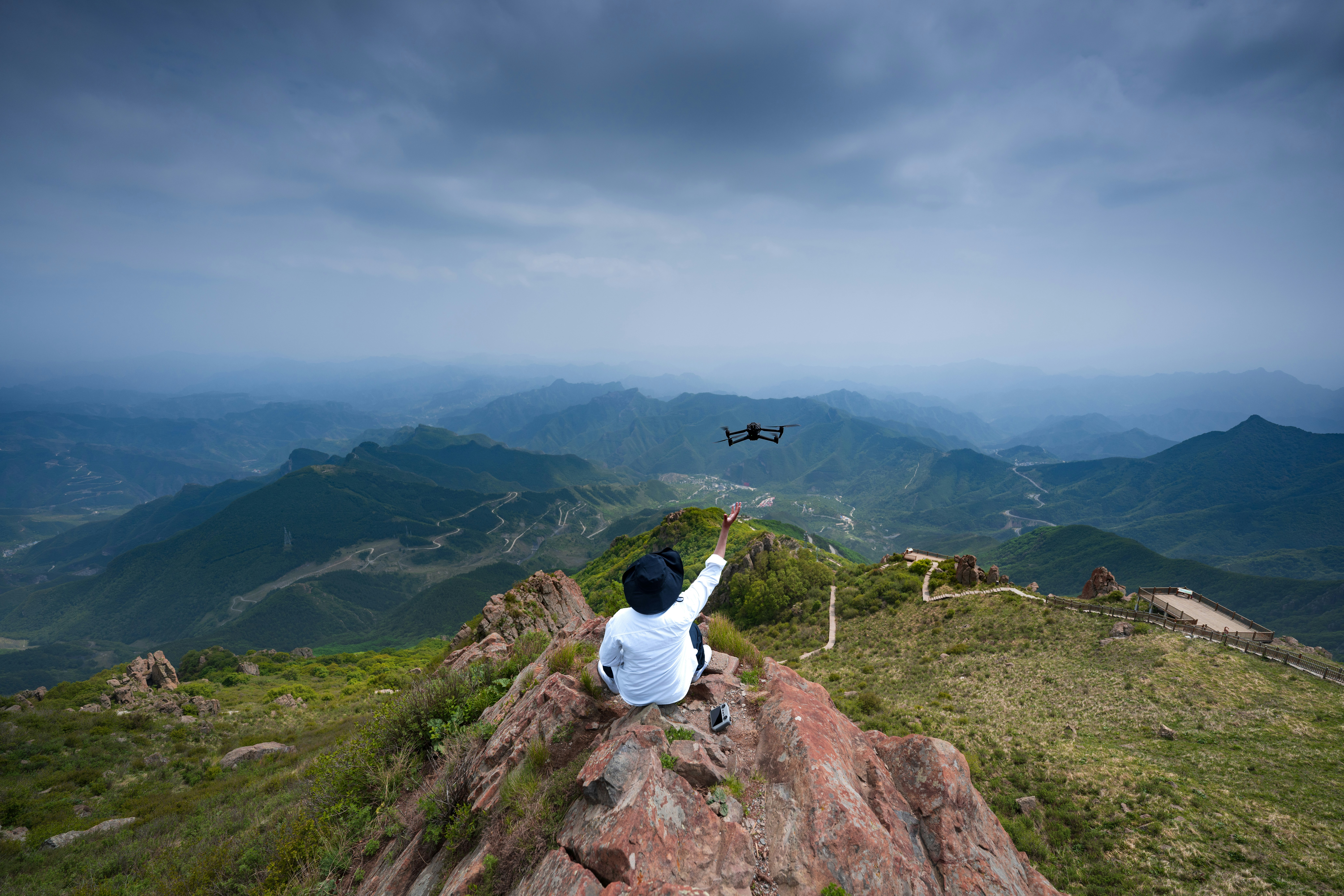 a person sitting on top of a mountain pointing at a helicopter