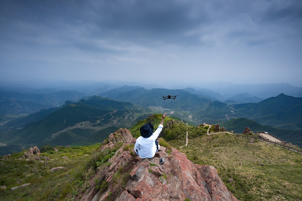 a person sitting on top of a mountain pointing at a helicopter