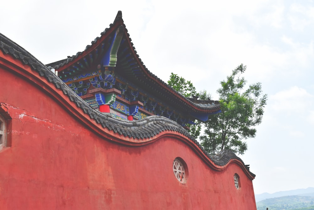 a red building with a blue roof and a tree in the background