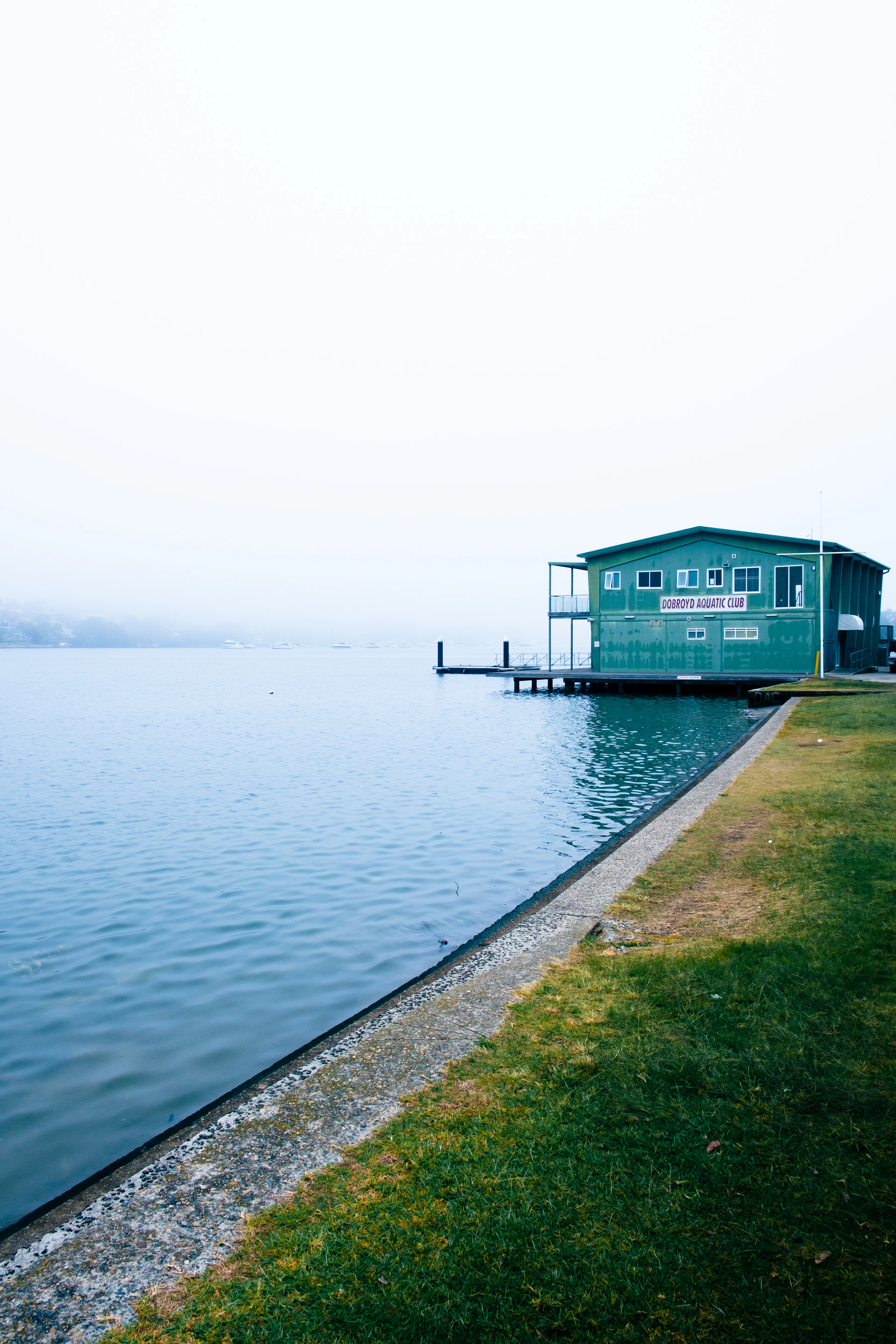 Blue boatshed at the edge of calm water on a misty morning