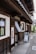 A traditional Japanese building with dark wooden panels and a white exterior. The entrance features a small sign with Japanese characters and a hanging fabric. A sidewalk runs alongside the building, leading to a sign with a portrait and an arrow directing visitors.