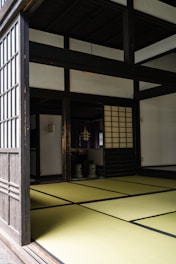 A traditional Japanese room with tatami mat flooring, sliding shoji doors, and a minimalistic interior. The space has a serene and orderly atmosphere, characteristic of traditional Japanese architecture.