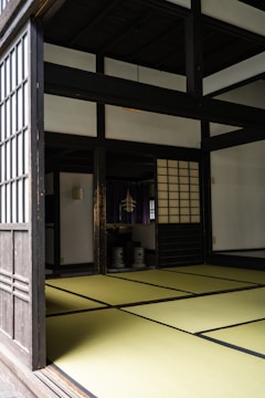 A traditional Japanese room with tatami mat flooring, sliding shoji doors, and a minimalistic interior. The space has a serene and orderly atmosphere, characteristic of traditional Japanese architecture.