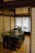 A traditional Japanese room featuring a dark wooden table set with green placemats, arranged on a tatami mat floor. The room is enclosed with shoji screens, creating a serene and minimalist atmosphere. Two wooden hangers are visible on the wall, adding to the rustic and organized aesthetic.