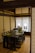 A traditional Japanese room featuring a dark wooden table set with green placemats, arranged on a tatami mat floor. The room is enclosed with shoji screens, creating a serene and minimalist atmosphere. Two wooden hangers are visible on the wall, adding to the rustic and organized aesthetic.