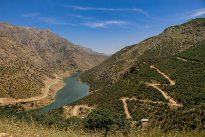 A winding river cutting through vibrant green hills under a clear blue sky.