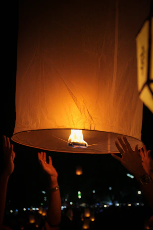 Hands releasing floating lanterns into the night sky during a temple festival, symbolizing hope and devotion.