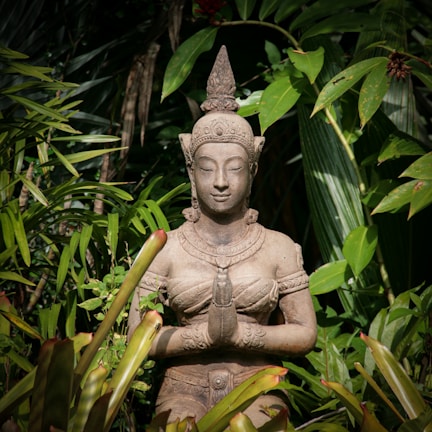 A serene outdoor scene with a statue of Ogum surrounded by offerings and flowers.