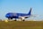 An airplane with a blue fuselage is on the runway, featuring the logo of ITA Airways on its side. The aircraft is positioned on a grassy field with a clear blue sky in the background, suggesting it's prepared for takeoff or has just landed.