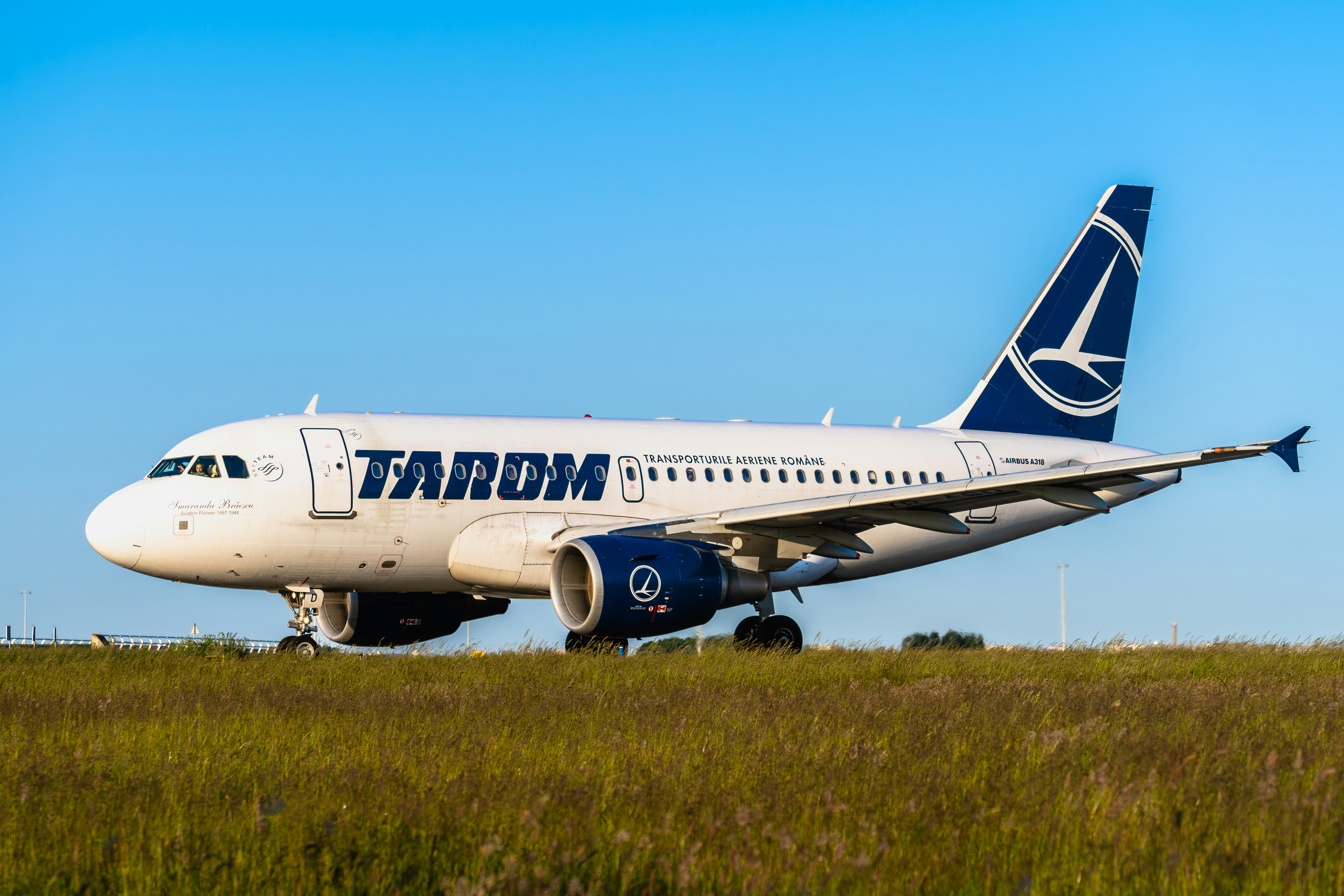 a large jetliner sitting on top of a lush green field, Tarom flight RO364 to Bucharest (an Airbus A318-111, reg. YR-ASD) taxiing to the Polderbaan runway at Schiphol airport for departure.