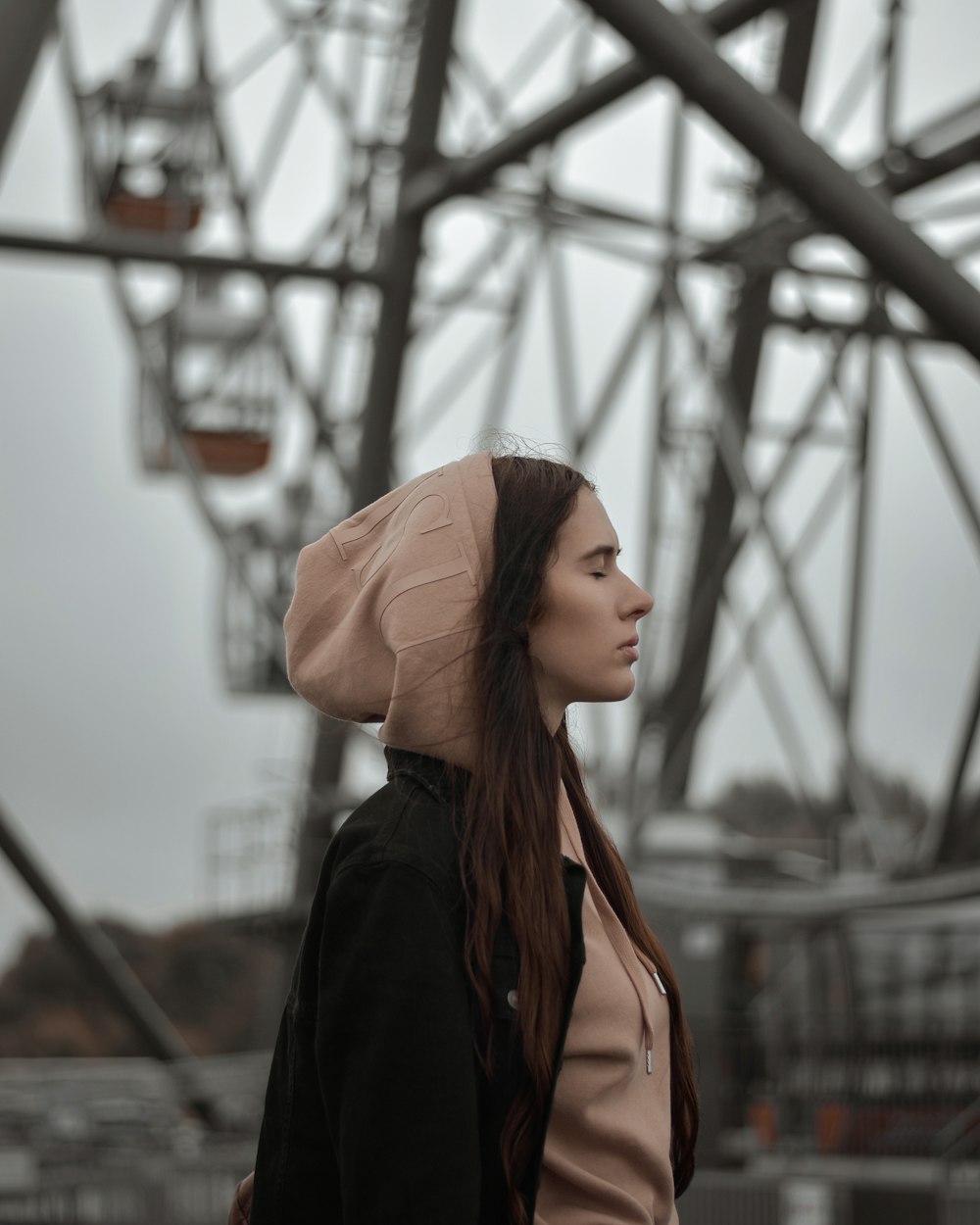 a woman with a hood on standing in front of a ferris wheel