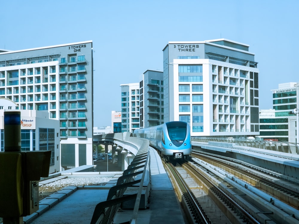a blue and white train traveling past tall buildings