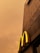 A concrete building facade with a prominent yellow letter 'M' extends upwards against a cloudy, sepia-toned sky.