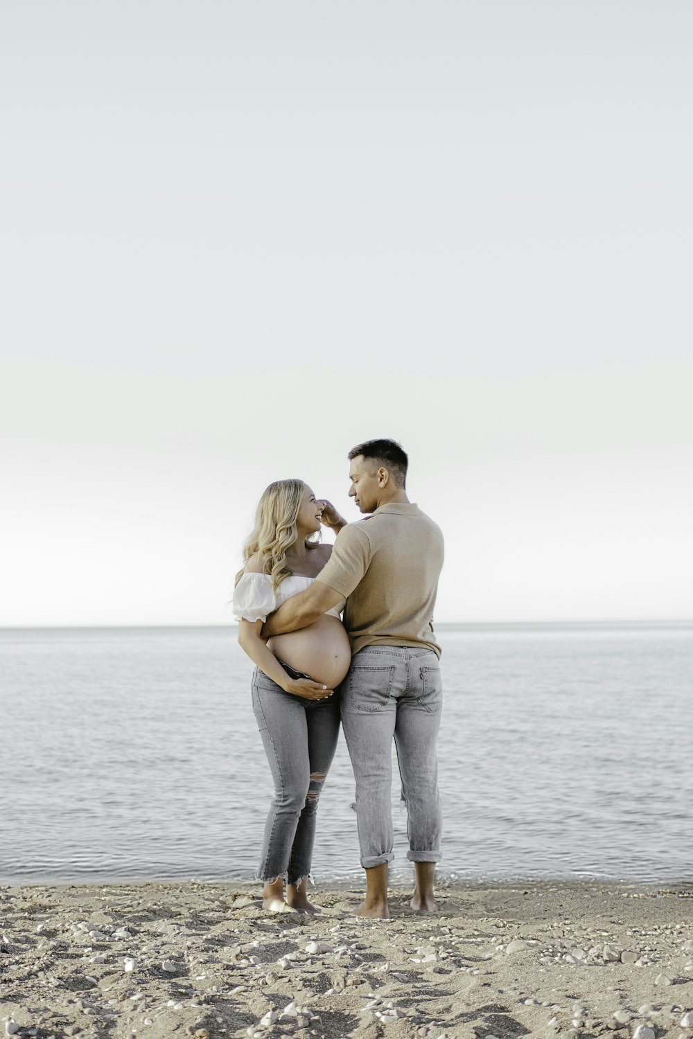 a man and woman standing on a beach next to the ocean
