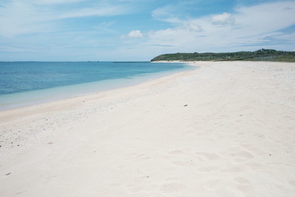 a sandy beach with blue water and a hill in the distance