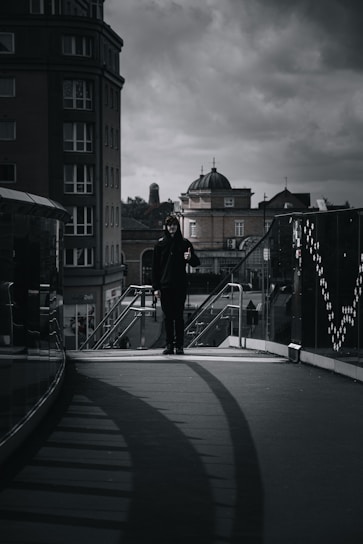 A moody urban scene featuring a man wearing layered dark streetwear with sharp, avant-garde details.