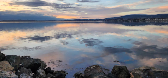 A serene lakeside at dawn with soft pastel skies reflecting calm and tranquility.