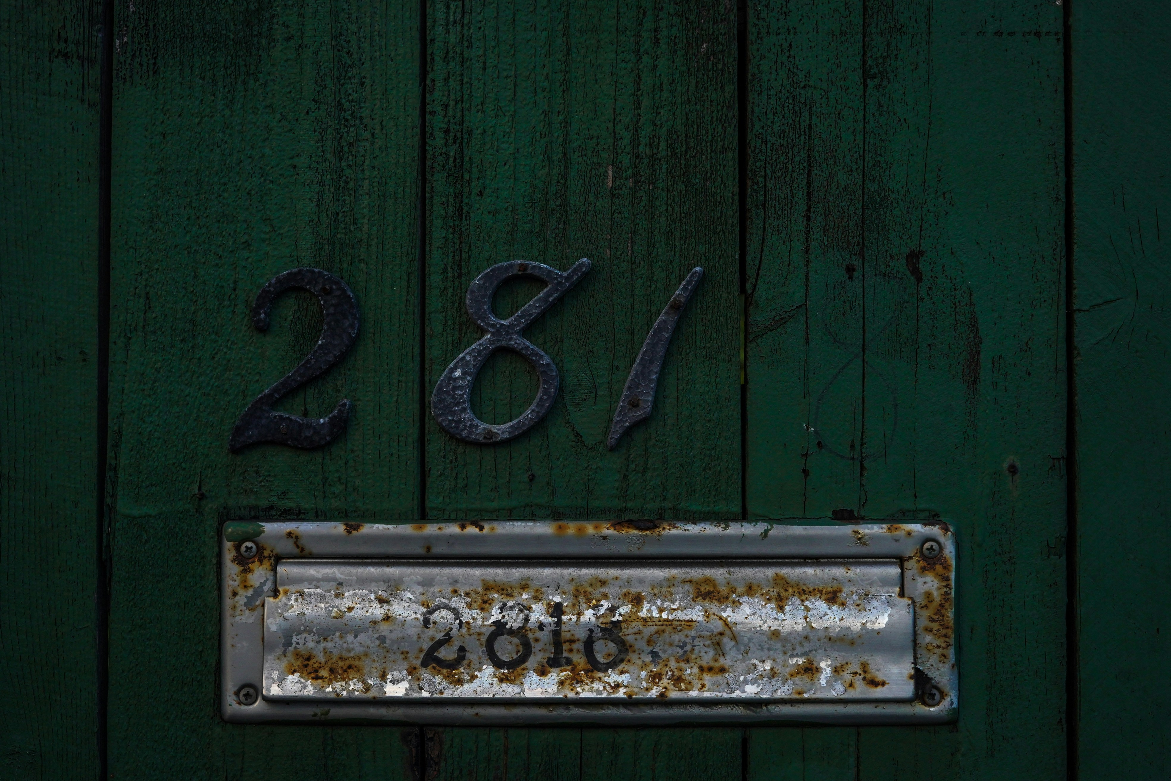 a green door with a rusted metal number plate