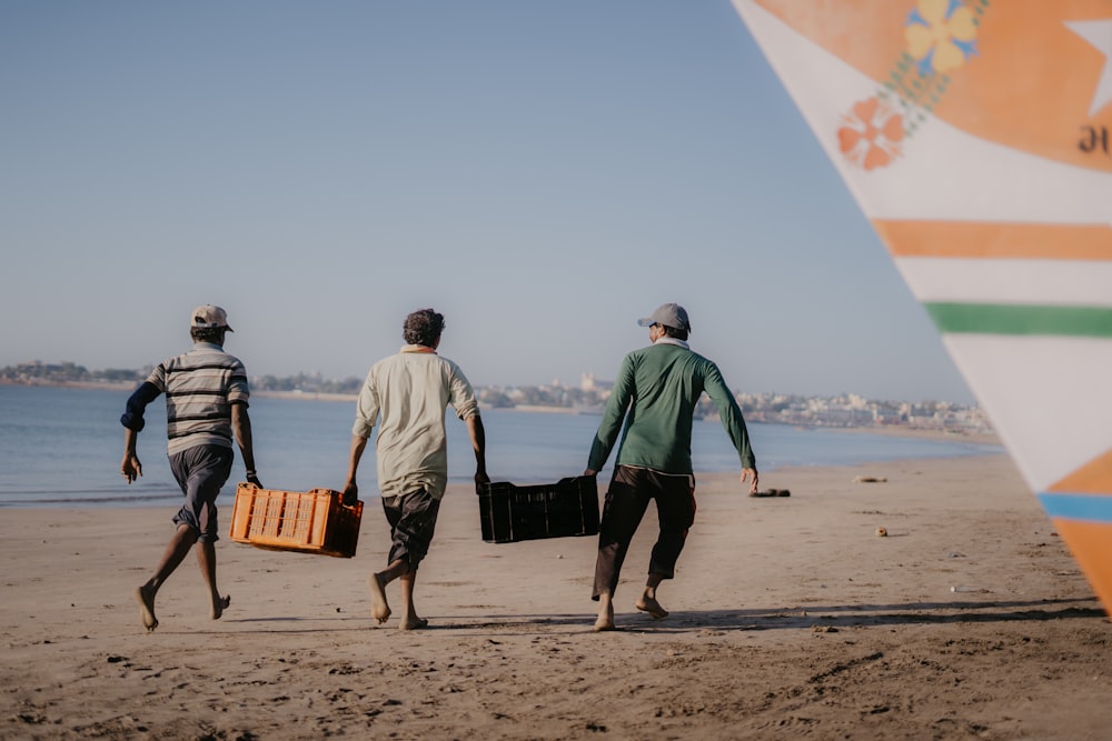 three men walking on a beach carrying luggage