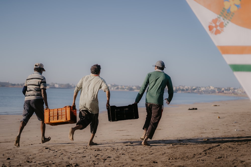 three men walking on a beach carrying luggage