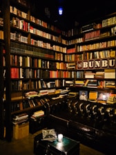 A cozy, softly lit library corner with worn leather chairs and shelves filled with aged, leather-bound books.