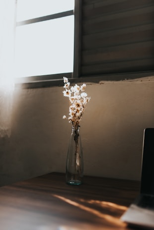 A serene home décor box featuring ivory and lavender flowers on a wooden table by a sunlit window.