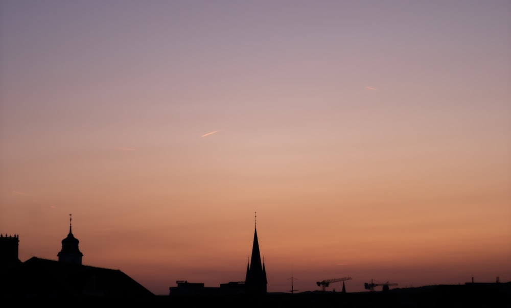 a sunset view of a church steeple with a plane in the sky