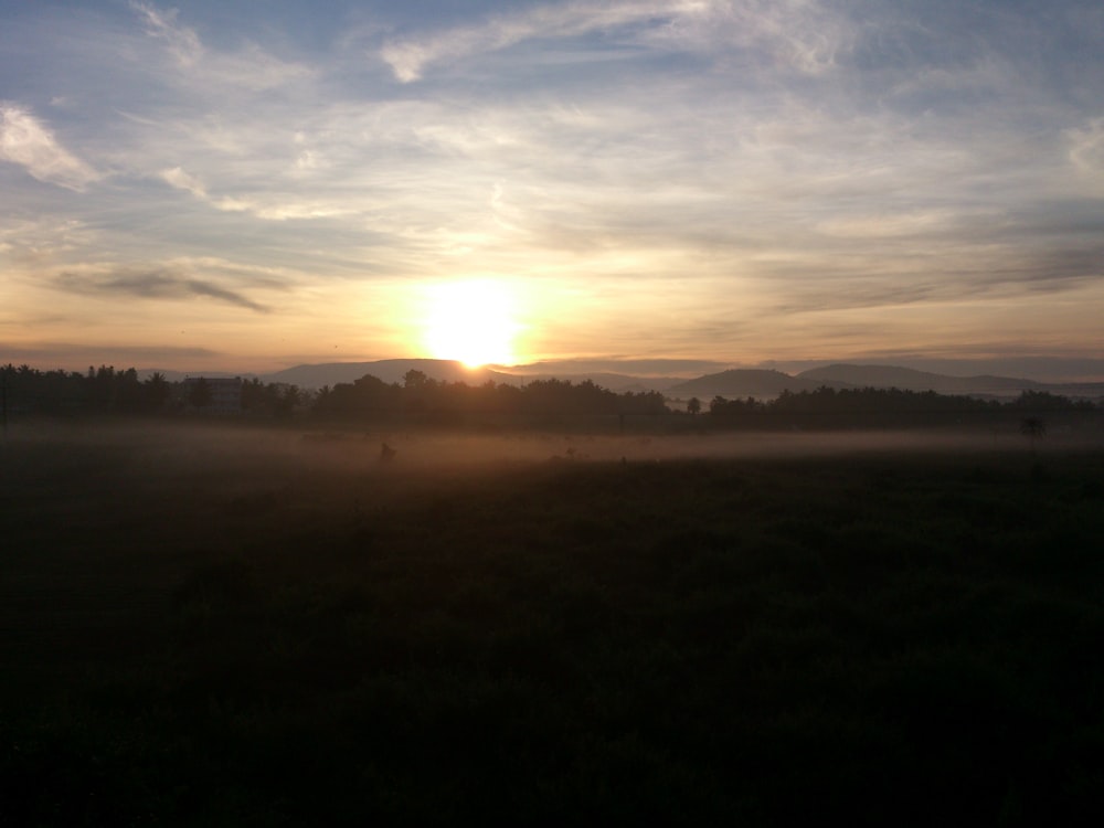 the sun is setting over a foggy field