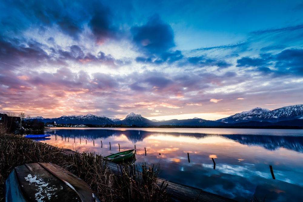 a boat sitting on the shore of a lake at sunset