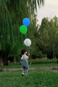 A close-up portrait of a smiling child holding a bunch of colorful balloons in a sunlit park.