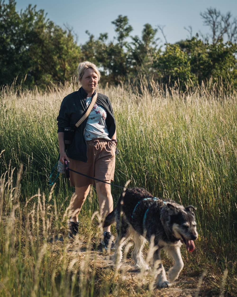 a woman walking a dog on a leash through tall grass