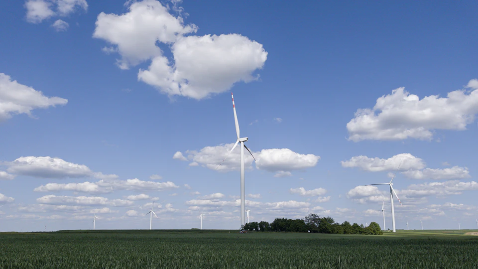 Large wind turbine stands tall against clear blue sky dotted with fluffy white clouds nearby