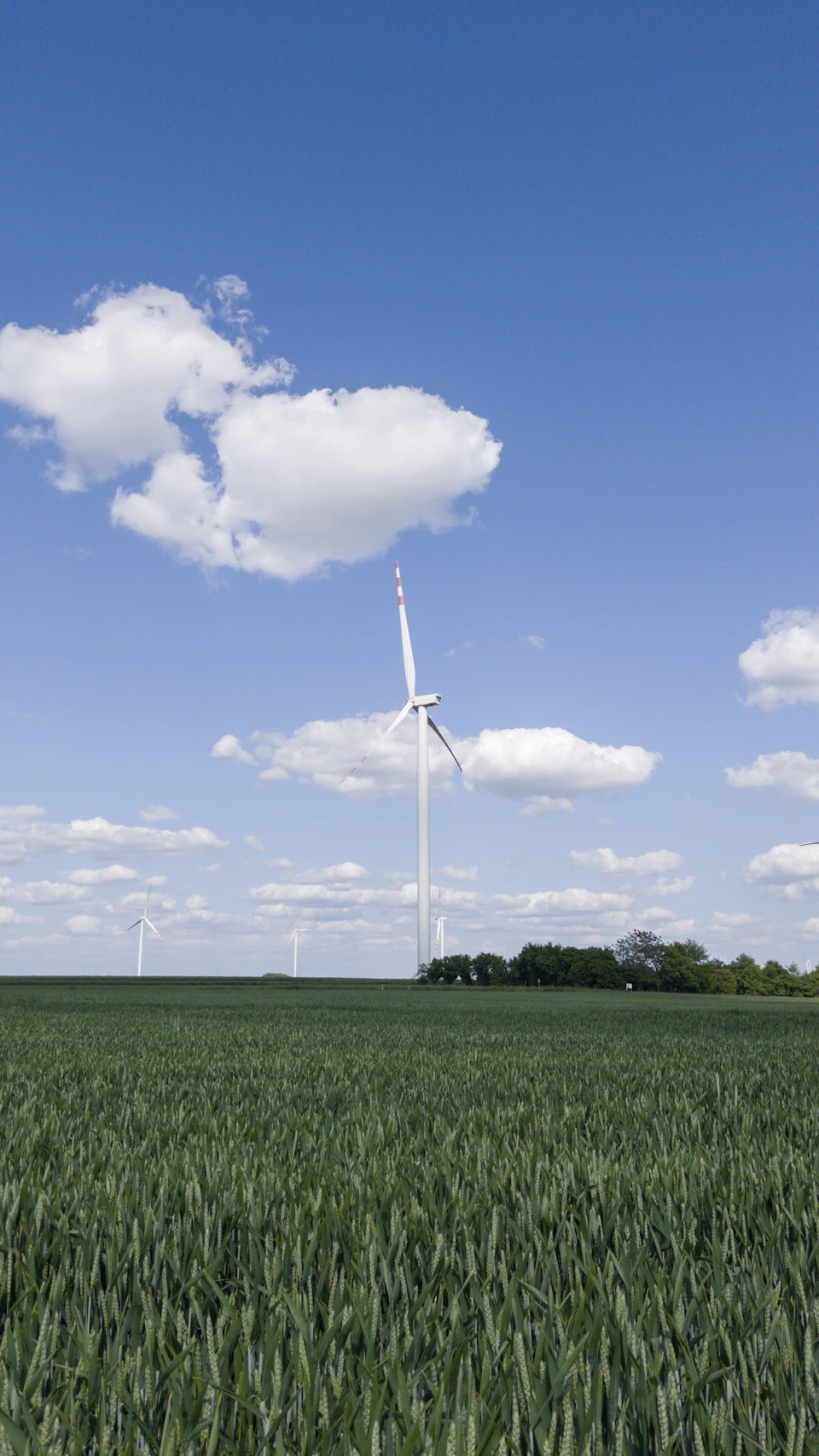 Large wind turbine stands tall against clear blue sky with fluffy white clouds nearby