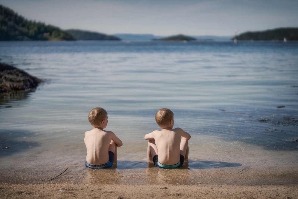 two young boys sitting in the water at the beach