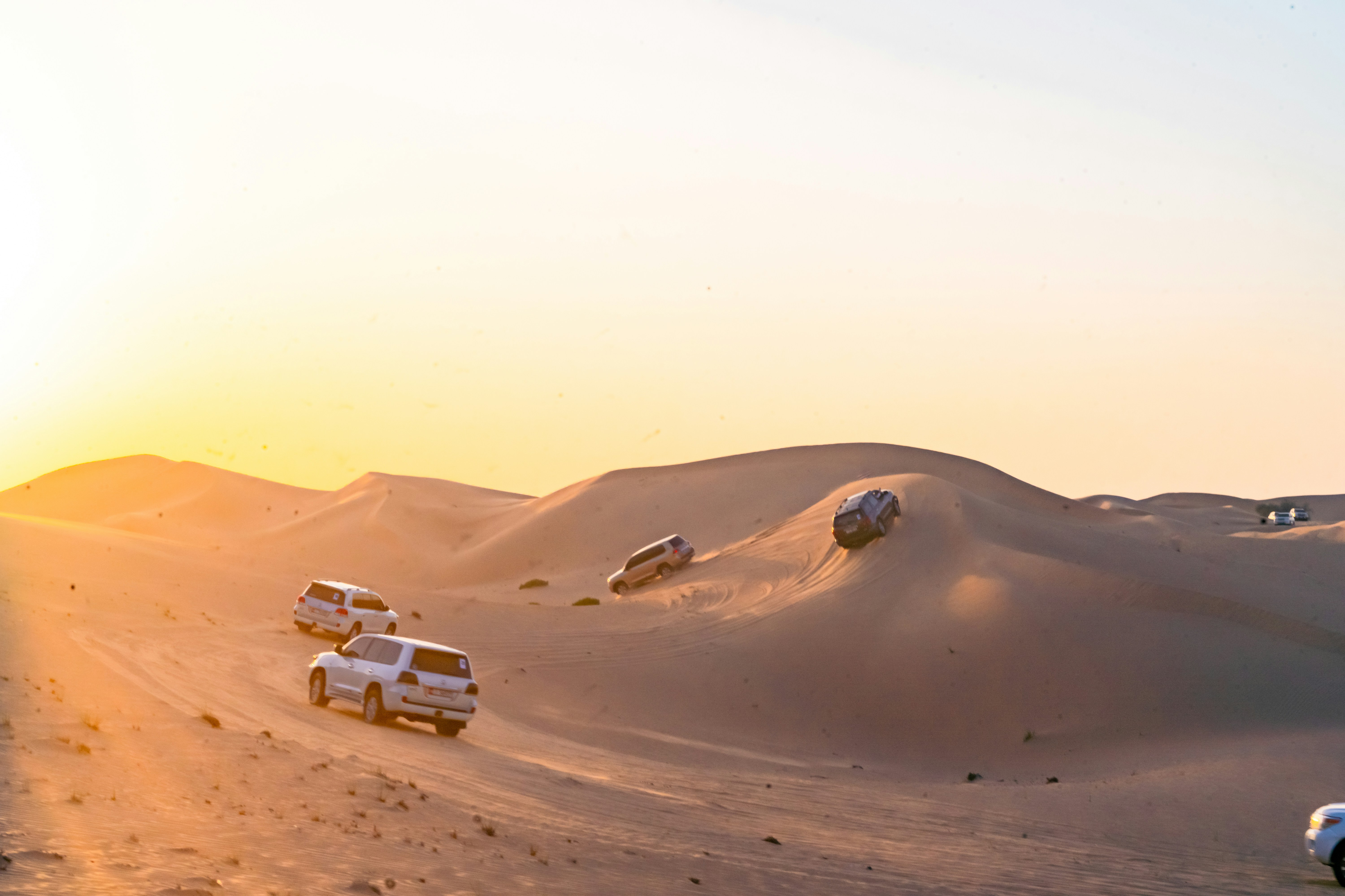 Zlate peščene sipine dubajske puščave ob sončnem zahodu s terenskimi vozili za safari