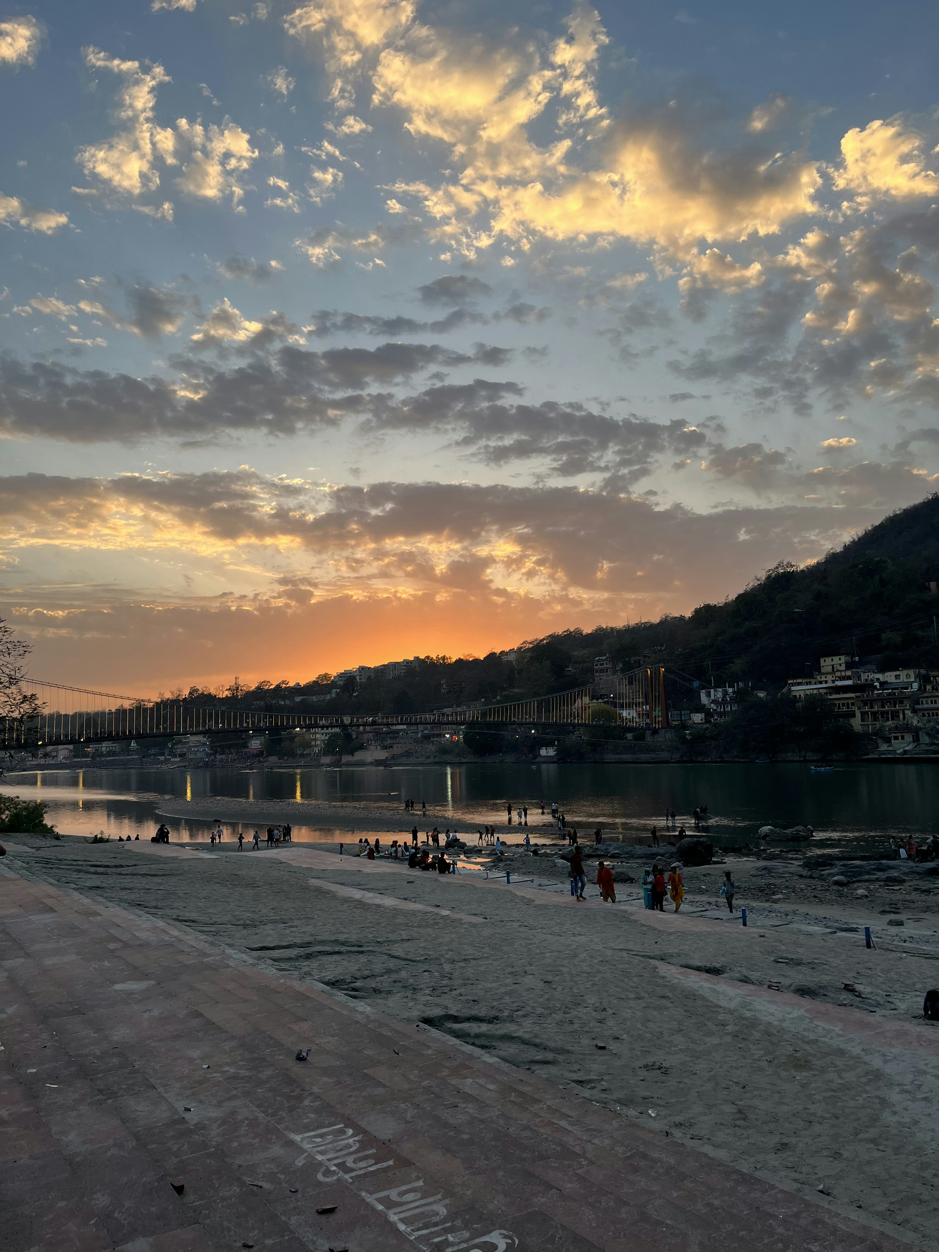 Rishikesh Ganga river with suspension bridge and yoga practitioners on the banks at sunset
