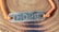 A metallic plate engraved with the word 'HOPE' is attached to an orange cord, forming a bracelet. The bracelet is placed on a surface with a wood-like pattern, highlighting the texture and color contrast between the metal, cord, and background.