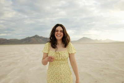 A smiling woman wearing a bright yellow dress standing in a sunlit city street.