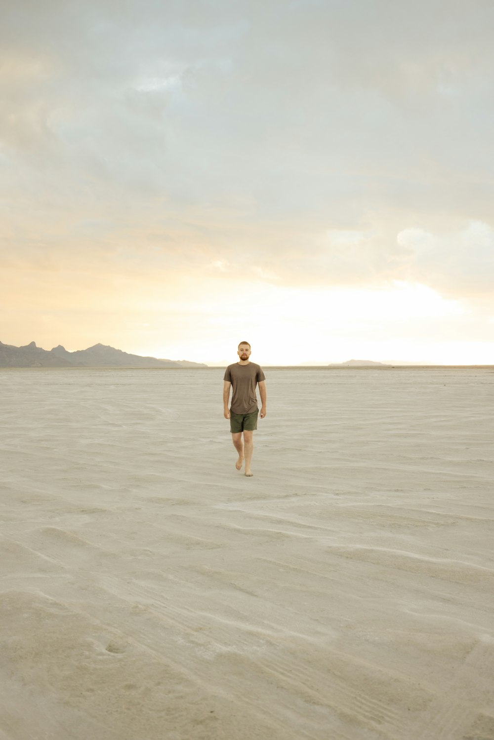 a man walking across a sandy plain under a cloudy sky