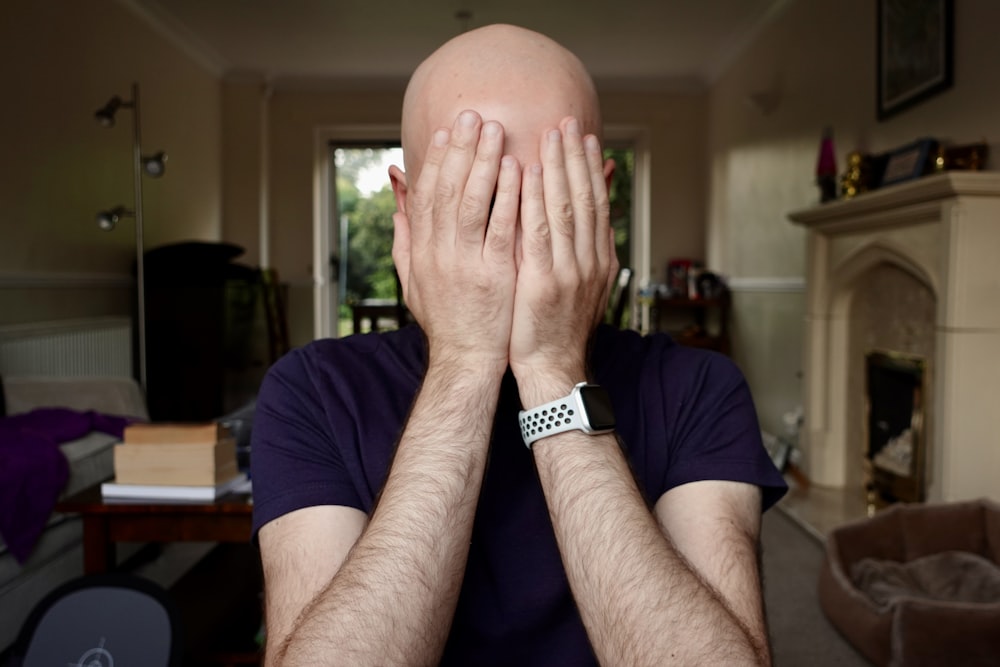 a bald man covering his face with his hands