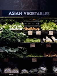 A grocery store display featuring a variety of Asian vegetables. The neatly arranged produce includes leafy greens such as bok choy and napa cabbage, as well as other items like ginger and daikon radishes. Price tags are visible, indicating different prices for the vegetables.