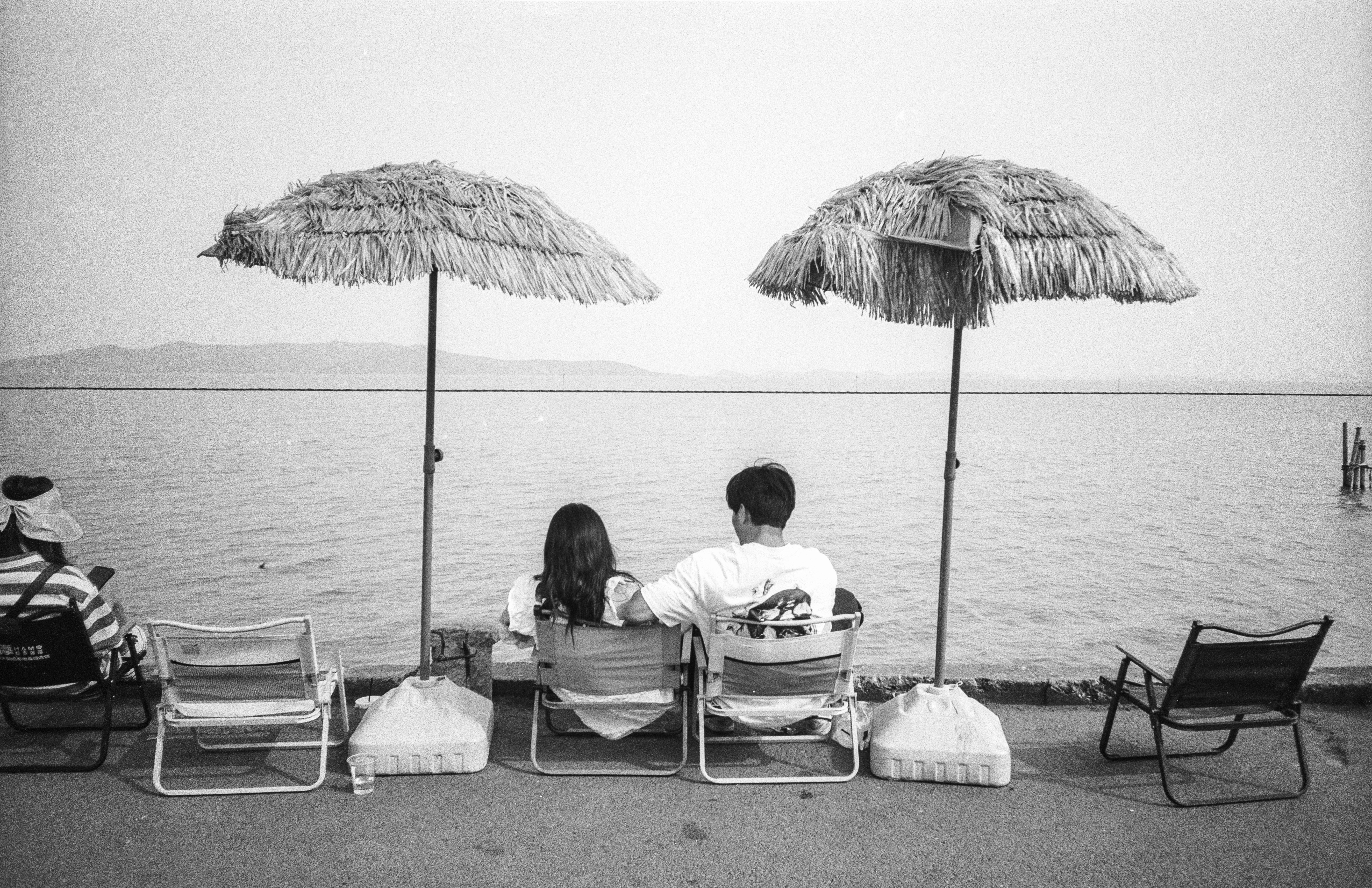 a man and a woman sitting on beach chairs under umbrellas
