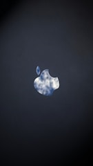 The image features a silhouette of an apple logo with a reflective sky pattern, revealing white clouds and a blue sky, set against a dark background.
