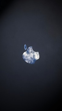 The image features a silhouette of an apple logo with a reflective sky pattern, revealing white clouds and a blue sky, set against a dark background.