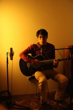 Michael Allen Howard playing guitar in a cozy recording studio surrounded by vintage microphones and warm lighting.