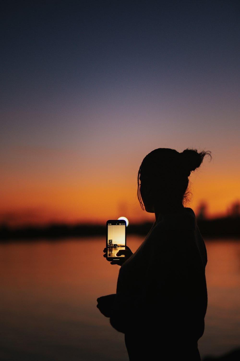 a person holding a cell phone in front of a body of water