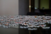 A close-up of a jigsaw puzzle on a table, with pieces scattered and some partially connected. The background is blurred, giving a focused perspective on the puzzle pieces, which display various colors and patterns.