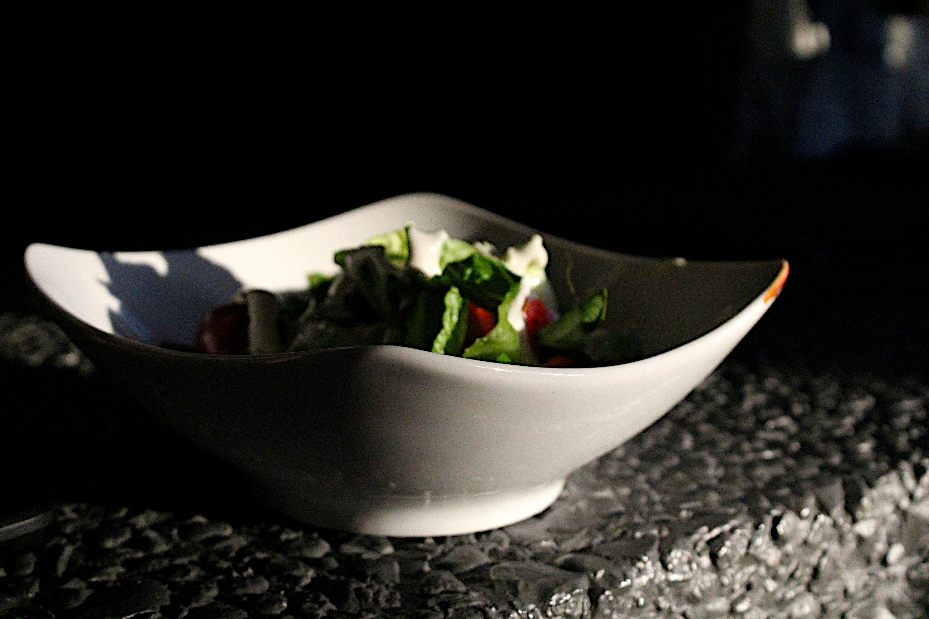 Colorful salad bowl with vegetables on dark wooden table, moody restaurant lighting