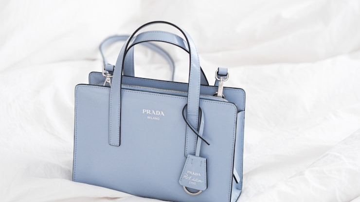 a blue prada bag sitting on top of a white sheet